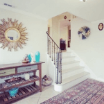 Landscape image of an entryway area with a console table and rug and mirror on the wall.