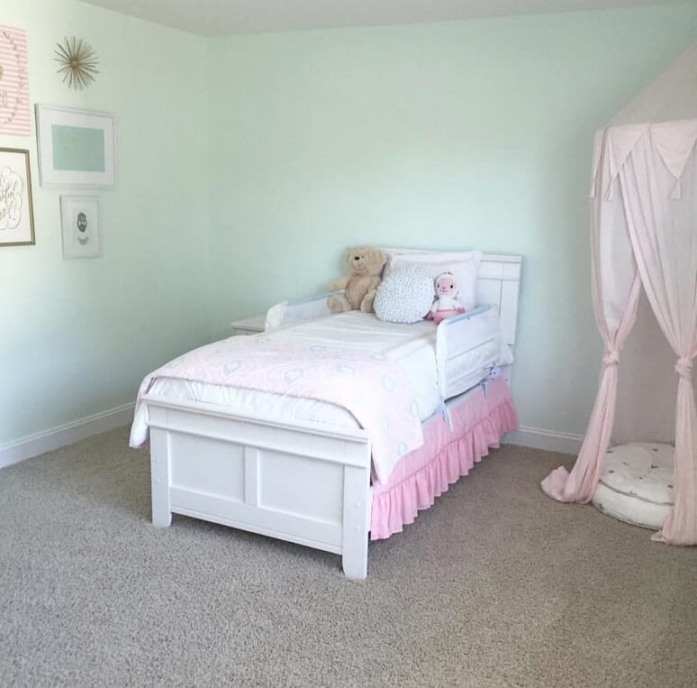 Image of the little girls room before the makeover. There is a white bed with a blank blue wall with a few frames on the wall. 