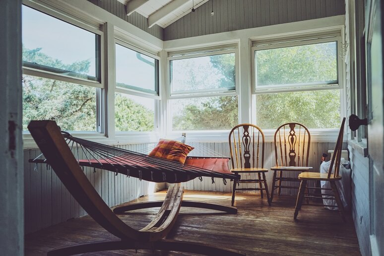 Photograph of a hammock in a sun room with large windows over looking the forest.